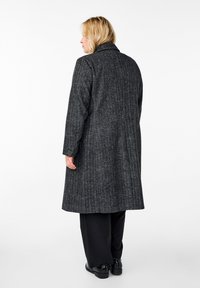 Cappotto grigio a quadri con colletto strutturato, maniche lunghe e un design di lunghezza media. Presenta un motivo testurizzato e una linea dritta.