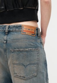 Κοντινό πλάνο στη μέση ενός ατόμου που φοράει ανοιχτό μπλε τζιν Diesel με δερμάτινη ετικέτα της μάρκας και τμήμα μαύρου κοντού τοπ ορατό.