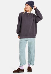Donkergrijs oversized sweatshirt, lichtblauwe geblokte broek, marineblauwe beanie, roze sokken en bruine klompen. Casual ontwerp met een relaxte pasvorm.