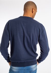 Marinblå bomullströja med rund halsringning, ribbade muddar och fåll, med en slät textur och standardpassform. Inga synliga logotyper.