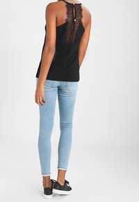 Černý top bez rukávů s krajkovým detailem na zádech, spárovaný se světle modrými skinny džíny a černými slip-on botami. Jednoduchý, přiléhavý design.