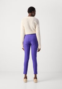 Pastelcrème fuzzy sweater en hooggeprijsde paarse broek met een taps toelopende pasvorm. Beige instapschoenen maken de outfit compleet.