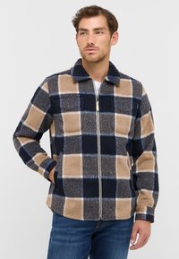 Plaid fleece jacket featuring beige, navy, and gray colors, a collar, zip closure, and two front pockets. Soft texture with a boxy fit.
