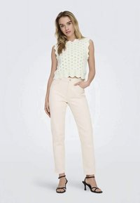 Top corto bianco lavorato a maglia con bordi a forma di scallop, abbinato a pantaloni beige chiaro a vita alta e tacchi neri con cinturini.