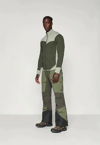 Zelená vonkajšia bunda s svetlosivými akcentmi, so zipsovým uzáverom, textúrovaná látka, kombinovaná so zelenými a sivými cargo nohavicami s vreckami.