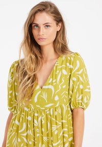 Grünes, gemustertes Kleid mit kurzen Puffärmeln, V-Ausschnitt und einem strukturierten Stoff mit weißen, abstrakten Designs.