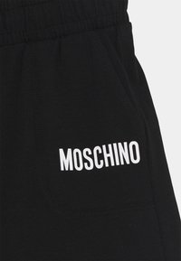 Schwarze Baumwoll-Jogginghose mit elastischem Bund, mit einem weißen "MOSCHINO"-Logo auf der Vorderseite der Tasche. Glatte Textur, schlichtes Design.