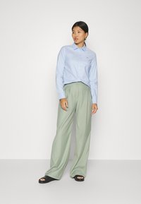 Heleda sinine nööpidega särk, rohelised laiad püksid, mustad libisemised sandaalid. Särgil on krae ja tikandiga logo. Sile kangamaterjal.