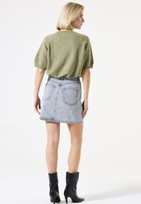 Pull court tricoté vert à manches courtes, mini-jupe en denim gris avec poches arrière et bottines noires à talons. Design simple et ajusté avec un ourlet brut.