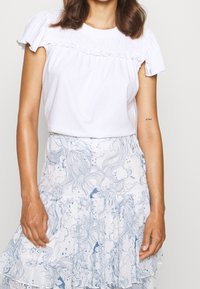 Vit kortärmad topp med volangdetaljer, matchad med en blå och vit mönstrad kjol med en flerlagrig volangnederkant.