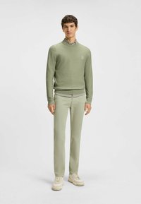 Jasnozielony sweter o fakturze z wysokim kołnierzem, założony na koszulę z kołnierzykiem. Połączony z pasującymi jasnozielonymi spodniami oraz beżowymi trampkami.