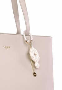 Šedá kožená totes taška s dvěma uchy, která má zdobený bílý prvek a dekorativní krémovou třásničku připevněnou zlatým řetízkem.