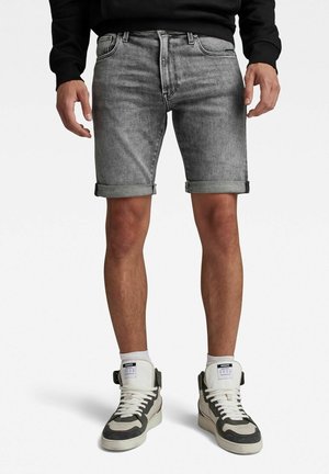Graue Jeansshorts mit umgeschlagenen Säumen, ausgestattet mit klassischem Fünf-Taschen-Design, dezentem Verblassen und mittelhoher Taille. Dazu hohe Sneakers.