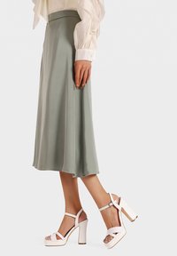 Gonna midi verde chiaro in tessuto liscio abbinata a sandali con tacco chunky bianchi, caratterizzati da una fascia e un design aperto sulla punta.