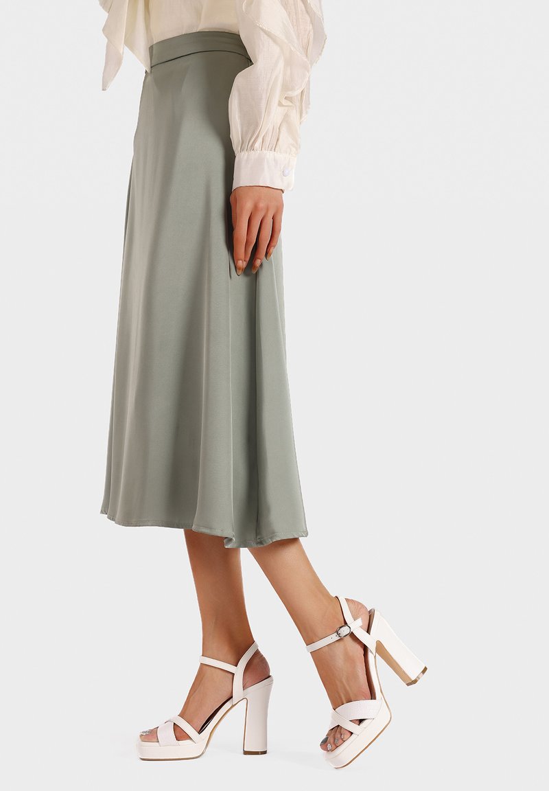 Gonna midi verde chiaro in tessuto liscio abbinata a sandali con tacco chunky bianchi, caratterizzati da una fascia e un design aperto sulla punta.