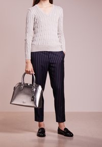 Pull gris clair à torsades avec col en V, associé à un pantalon bleu marine à fines rayures. Sac à main argenté métallisé avec un design structuré et des ferrures.