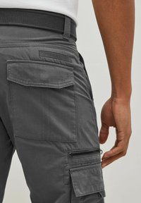 Cargo pants in dark gray fabric with multiple pockets. Features include a smooth texture, side zipper pocket, and a woven belt for adjustment.