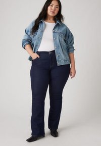 Lyseblå denimjakke over en hvit topp, kombinert med mørkeblå vide jeans. Jevn tekstur, figurnær silhuett og minimale metalliske detaljer.