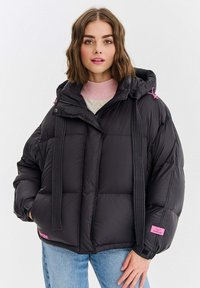 Czarna pikowana kurtka puchowa z kapturem, przeszyciami i różowymi akcentami. Kurtka zapinana na zamek z przodu, zestawiona z jasnoróżowym swetrem.