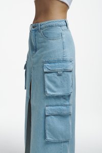 Svetlo modra denim krilo cargo z stranskimi razporki, velikimi zakrpami in visokim pasom, ki vključuje klasičen gumb in zadrgo.