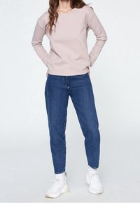 Pull en laine rose clair à col rond associé à un jean bleu foncé. La tenue est complétée par des baskets blanches, créant un look décontracté.