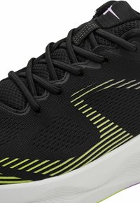 Chaussure de sport noire avec des lacets noirs, un design rayé vert citron sur la tige en tissu, une semelle blanche, et un petit logo violet sur la languette.