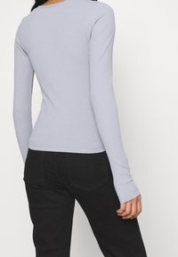 Hellblau-lavendelfarbenes, geripptes Langarmoberteil mit rundem Halsausschnitt und taillierter Silhouette, kombiniert mit hoch taillierten schwarzen Jeans.