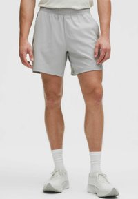 Lichtgrijze sportshorts met een elastische tailleband, zijzakken en een gestructureerde stof. Gecombineerd met witte sokken en sneakers.