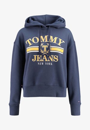 Tmí modrá zkrácená mikina vyrobená z bavlny, která má kapuci se šňůrkami a žlutý text "TOMMY JEANS NEW YORK" s grafickým logem uprostřed.