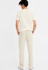 Lysfarvet, tekstureret strik kortærmet skjorte parret med beige linnedbukser og lyse sneakers, set fra ryggen.