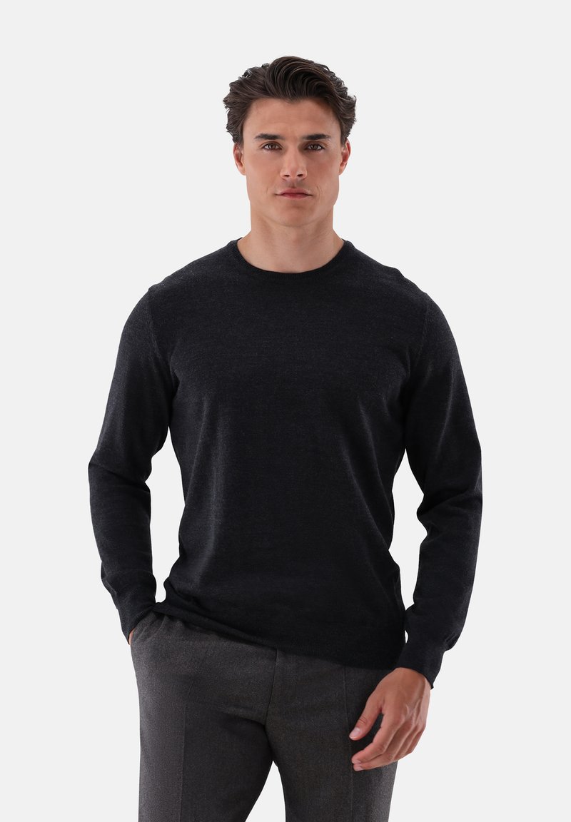 Schwarzer Pullover mit langen Ärmeln aus einem weichen Stoff, rundem Ausschnitt, taillierter Silhouette und gerippten Bündchen, kombiniert mit grauen Hosen.