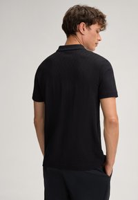 Schwarzes Polo-Shirt mit kurzen Ärmeln und einem strukturierten Wellenmuster. Mit klassischem Kragen und komfortablem Sitz. Geeignet für die Freizeit.