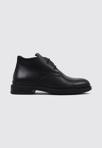 Botas de tobillo de cuero negro con un acabado suave, puntera redondeada, dos ojales para los cordones y una suela de goma texturizada y baja.
