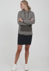 Hettegenser i mørkegrå med hvite horisontale striper, har en frontlomme og snøring. Kombinert med en marineblå skjørt og hvite sneakers.