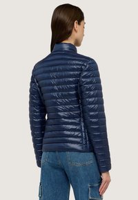 Giacca puffer blu navy con finitura lucida, dotata di colletto rialzato e design a righe orizzontali. Abbinata a pantaloni cargo in denim blu.