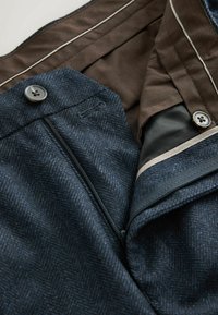 Pantalons noir bleu à chevrons avec une doublure marron, comportant une fermeture à bouton, une poche zippée et des accents de bandes légères le long de la taille.