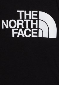 Camiseta de algodón negra con texto blanco en negrita "THE NORTH FACE" y un diseño de semicírculo, textura suave, corte casual.