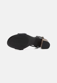 Sorte hæl sandal med en tekstureret gummisål, der har en glat overdel og en blokhæl med en naturlig træaccent.