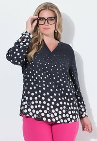 Maglietta nera con scollatura a V e maniche lunghe, decorata con pois bianchi di diverse dimensioni, abbinata a pantaloni rosa.