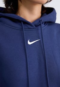 Mørkeblå Nike hettegenser med frontlomme, snor i hetten og hvit logo på brystet. Mykt stoff med en jevn tekstur.
