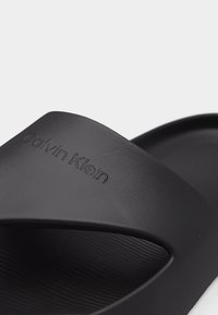 Μαύρο σανδάλι slide Calvin Klein με φαρδιά λουρί με ανάγλυφο το όνομα της μάρκας και υφή στο πέλμα.