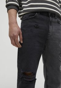 Jeans in denim nero con strappi. Presentano un classico design a cinque tasche, una leggera scoloritura e dettagli di cucitura visibili.