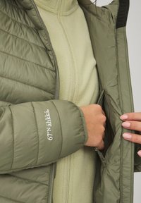 Grøn quilted jakke med en indvendig lomme, parret med en lys grøn fleece-top. Funktioner inkluderer en højt krave og glat tekstur.