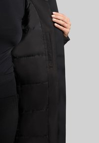 Sort pufferjakke med en glat ydre skal og quiltet inderside. Har et strømlinet design med en skjult lomme indeni.