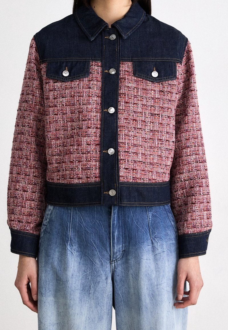 Chaqueta corta con un cuello y puños de mezclilla oscura, con un patrón tejido en rojo y blanco, botones plateados y dos bolsillos frontales.