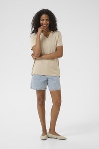 T-shirt beige à col en V, short en denim bleu clair avec broderies florales et ballerines beiges. Look décontracté et confortable, idéal pour les temps chauds.