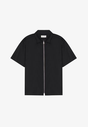 Chemise noire à manches courtes avec un col net et une fermeture éclair sur le devant. Tissu lisse avec un léger éclat, sans motifs ni accents visibles.