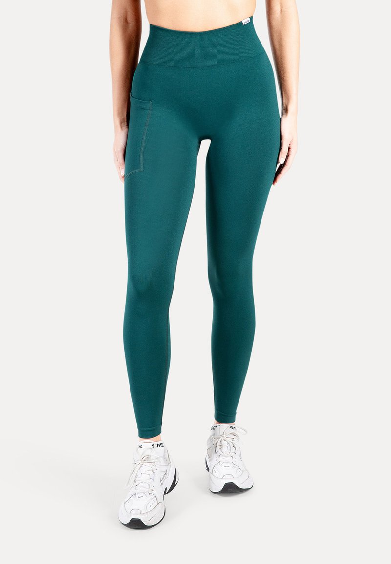 Leggings met hoge taille in zeegroen, gemaakt van rekbare stof, voorzien van een zijzak en een gladde textuur, gecombineerd met witte sportschoenen.