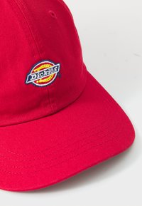 Piros pamut sapka ívelt silddel, a frontrészen színes hímzett "Dickies" logóval. A sild szegélyén varrott részletek.