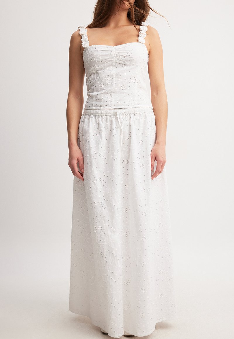 Weißes Maxikleid mit einem figurbetonten Oberteil, Rüschenträgern und einem elastischen Taillenbund. Der Stoff hat eine florale Stickerei und eine leichte Textur.
